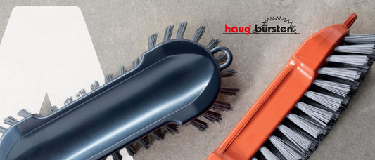 Banner mit zwei Haug Bürsten Scheuerbürsten auf einem Grauen Betonartigen Hintergrund. Inklusive Logo Haug Bürsten