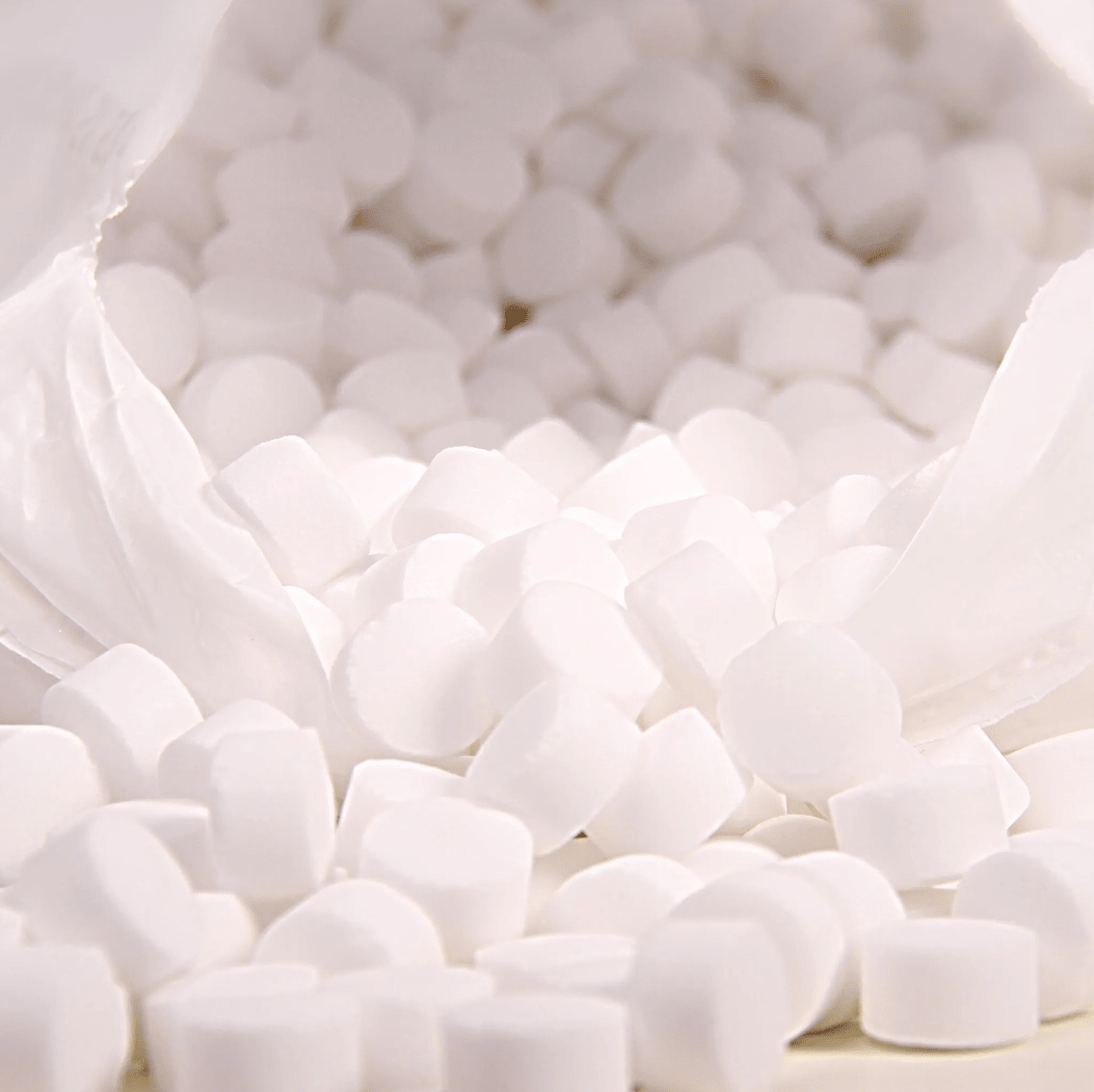 A close-up shows a white plastic bag labeled “K+S Minerals and Agriculture GmbH” containing Regenit evaporated salt tablets (EN 973 Type | Bag, 25 kg) falling onto a surface. The small, round tablets are uniform in shape and size and are ideal for use in water softening systems.