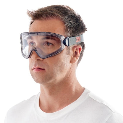 A man is wearing the 3M™ Safety Glasses 2891 with Scotchgard™ Protector Anti-Fog, indirectly vented and clear lens, manufactured by 3M Deutschland GmbH. The glasses have a black and gray adjustable strap and are pictured against a white background.