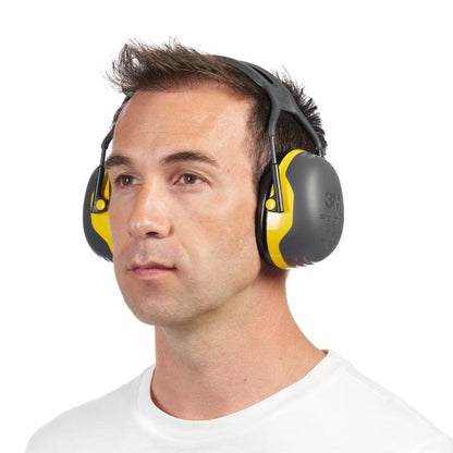 A man in a white shirt wears 3M™ PELTOR™ Comfort Earmuffs from 3M Deutschland GmbH and looks straight ahead with a neutral expression.
