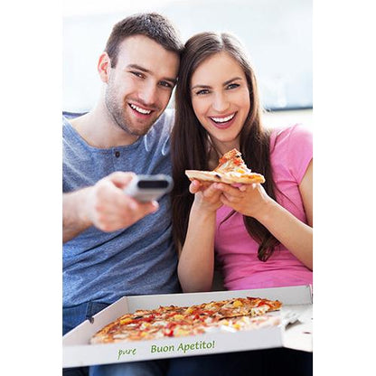 A cheerful couple relaxes on a sofa. In front of them is an open PAPSTAR 100 pizza box, cellulose "pure" square from PAPSTAR GmbH. He holds a remote control in his hand, she enjoys a piece of pizza. Both look happy.