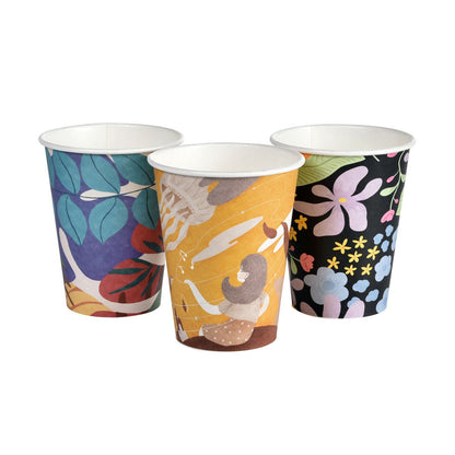 Three Art Series coffee mugs from Duni GmbH: PAP/PLA printed with blue, purple leaves, a seated person on yellow, and colorful flowers on black - stylish, biodegradable, and environmentally friendly.