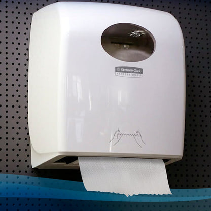 A wall-mounted white Kimberly-Clark GmbH Scott® Control™ Slimroll™ dispenser holds visible paper towels and features a transparent window and hand drying instructions on the front; installed on a perforated wall (6 rolls/carton, white).