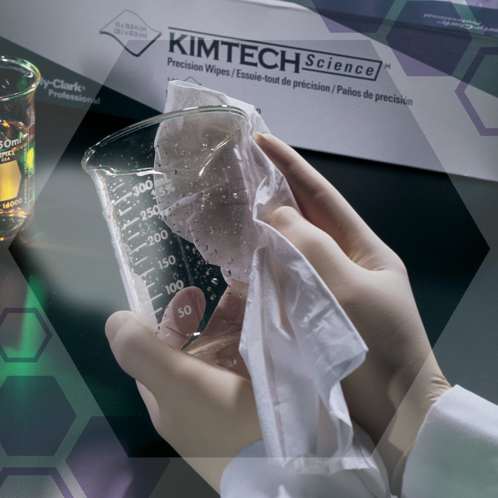 Eine Person mit weißen Handschuhen wischt einen Klarglasbecher mit Kimtech® Science Präzisionswischtüchern der Kimberly-Clark GmbH ab. Im Hintergrund stehen eine Schachtel mit den Tüchern (100 Blatt, 2-lagig) und ein Becher mit Flüssigkeit.