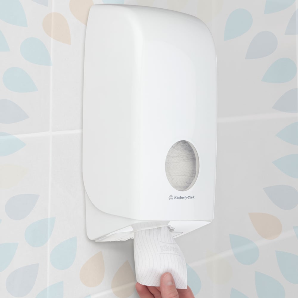 A hand pulls a sheet from a wall-mounted Kleenex® toilet paper single sheet system (Kimberly-Clark GmbH), white, 200 sheets per pack, 36 packs, in a bathroom with patterned tile walls.