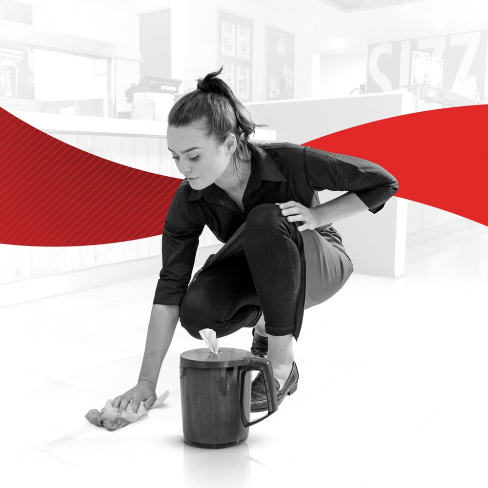 A woman in dark clothing kneels and wipes the floor with a WypAll® Reach™ paper towel for food & hygiene - centerfeed from Kimberly-Clark GmbH. A bold red curve on a black-and-white background emphasizes the importance of hygiene.