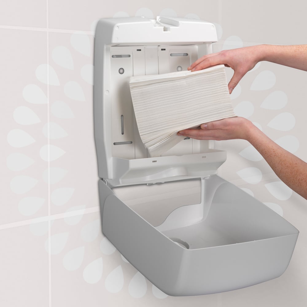 A person loads a stack of Kimberly-Clark GmbH Kleenex® Ultra™ Hand Towels MultiFold (White, Small, 18 Clips x 150 Sheets) into a wall-mounted paper towel dispenser in a restroom.