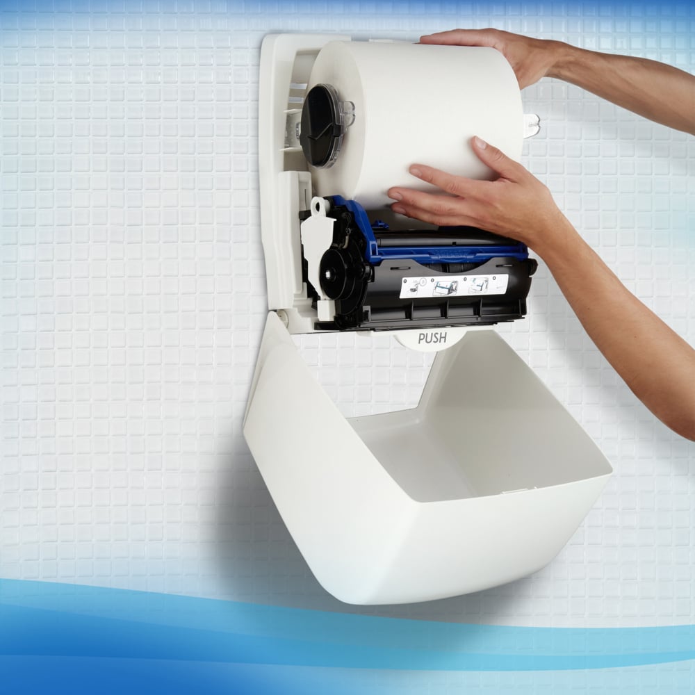 Eine Person installiert ein Scott® Control™ Handtücher - Rolle / Weiß der Kimberly-Clark GmbH in einem Wandspender an einer gefliesten Wand zum hygienischen Händetrocknen.