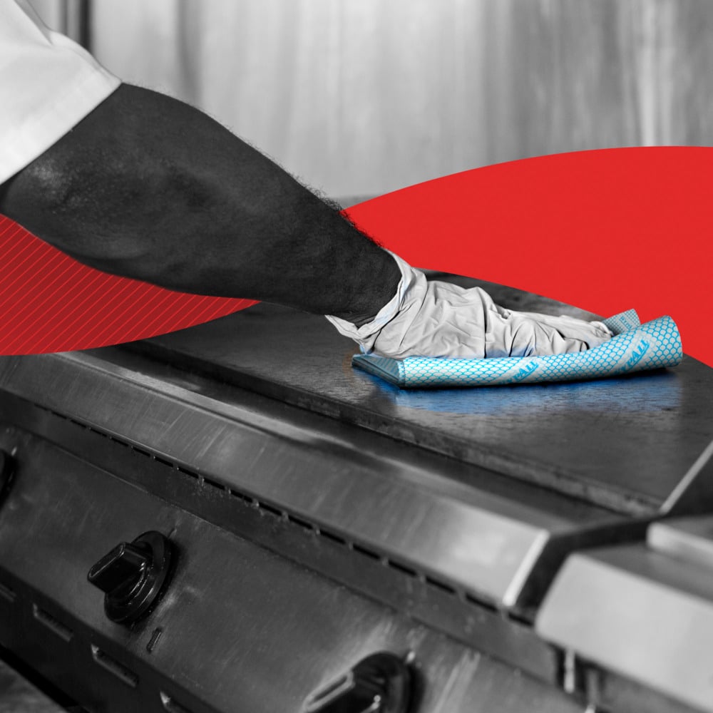 A person with gloves wipes a metal stove top with a blue WypAll® X50 Wiper - Interfold cloth (41.80 cm x 24.70 cm) from Kimberly-Clark GmbH. A red curved graphic in the background emphasizes the cleanliness and care of the kitchen.