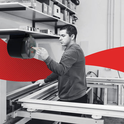 In a workshop, a person extracts a WypAll® L20 paper towel from Kimberly-Clark GmbH via central dispensing from the wall dispenser and cleans industrial work surfaces; a red graphic element runs through the center of the image.