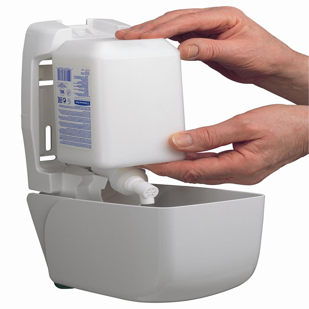 Two hands insert a 1L Kleenex® moisturizing hand and body lotion cassette by Kimberly-Clark GmbH into a wall-mounted white dispenser, providing convenient access to the moisturizing lotion for hand and body care.
