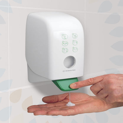 A person dispenses Kleenex® moisturizing hand and body lotion (Kimberly-Clark GmbH) from a white 1-liter wall cassette in a tiled bathroom with a green lever for hand and body care. Package: 6 cassettes per carton.
