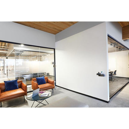 Limistéar feithimh oifige nua-aimseartha le dhá chathaoir leathair dhonn, piliúir ghorma, bord caife gloine le ríomhaire glúine agus leabhar nótaí agus seomraí cruinnithe gloine atá feistithe le dromchla cláir bhána Post-it® Easy Erase de chuid 3M Deutschland GmbH.