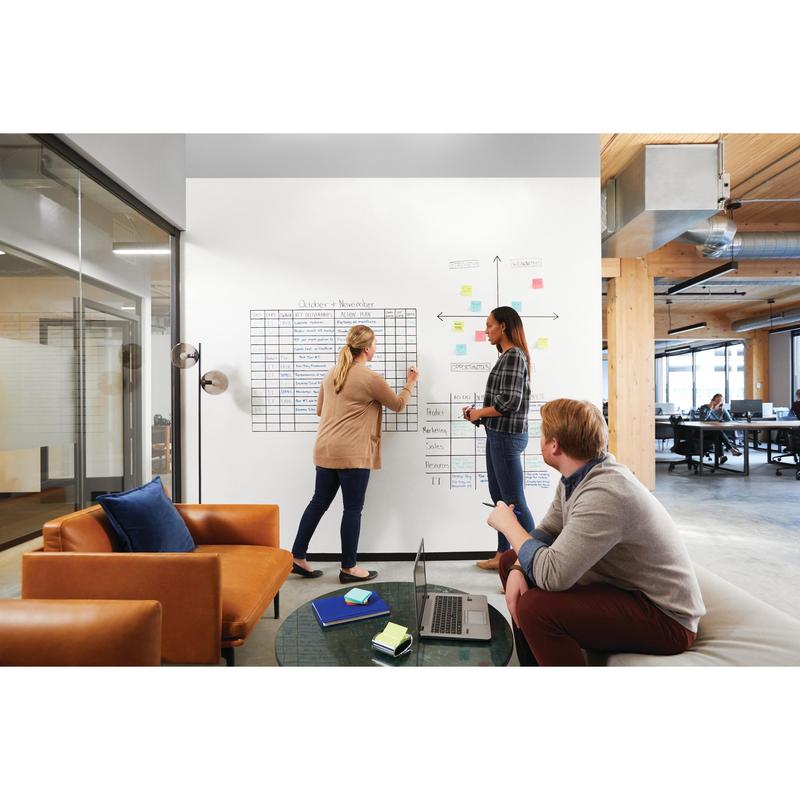 Tá triúr daoine ina suí in oifig nua-aimseartha. Tá beirt ag úsáid an dromchla cláir bhána Post-it® Easy Erase, bán ó 3M Deutschland GmbH, agus ag cur cairteacha agus nótaí greamaitheacha leis; tá duine amháin ina shuí ar tolg le ríomhaire glúine. Tá fuinneoga móra agus limistéar oibre oscailte le feiceáil.