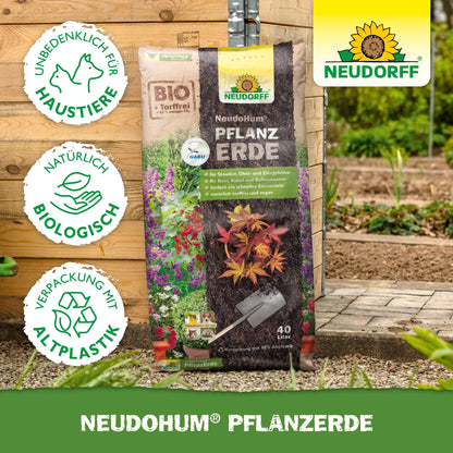 A bag of NeudoHum Plant Soil from the Neudorff Shop stands upright in a garden, perfect for perennials and shrubs. The symbols show that it is organic, cruelty-free, peat-free, and made from recycled plastic; the Neudorff logo is in the upper right corner.