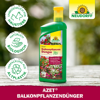 Auf einem Tisch steht eine Flasche Neudorff Shop Azet BalkonpflanzenDünger flüssig mit Symbolen für Haustiere, Bio und Biokunststoff; im Hintergrund blühende Sommerblumen, Balkonkästen und das Neudorff-Logo.