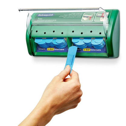 A hand pulls a bandage from a green Salvequick X-ray detectable plaster dispenser (Orkla Wound Care AB), which contains 2x30 plaster refills, with additional bandages visible inside the dispenser.