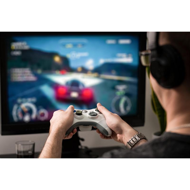 With headphones on, a gamer plays a car racing game with a red sports car on a large monitor. Nearby, the Scotch® Extremium™ INVISIBLE High-Performance Tape (20 m x 48 mm) from 3M keeps the cables organized and out of the way.