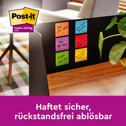 On a computer monitor are six colorful Post-it® Super Sticky Notes (76 mm x 76 mm, 90 sheets/block) from 3M Deutschland GmbH with handwritten names and numbers. In the background, a plant, a chair, and a table can be seen. German text below.