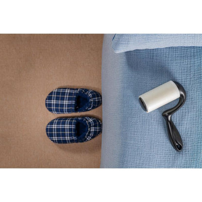 A pair of blue checkered slippers stands on a beige carpet next to a bed with a light blue bedspread, while the 3M Deutschland GmbH Scotch-Brite™ Everyday Clean Lint Roller for flat surfaces (56 sheets, 1/package) lies on the bed ready for use.