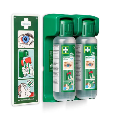 Two 500 ml eye wash bottles from Orkla Wound Care AB are mounted in a wall holder (for eye wash 500 ml, 1 piece); a glowing instruction sign for emergency use is included.
