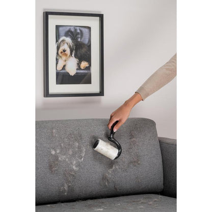 Using the Scotch-Brite™ Everyday Clean Lint Roller for flat surfaces (56 sheets, 1/package) from 3M Deutschland GmbH, someone removes pet hair from a gray fabric sofa under a photo of a dog.
