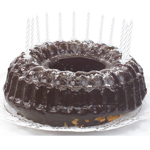 A chocolate cake with shiny glaze, decorated with PAPSTAR GmbH birthday candles 6 cm, white with holder (24 pieces), which are evenly distributed around the edge and lie on a white lace doily.