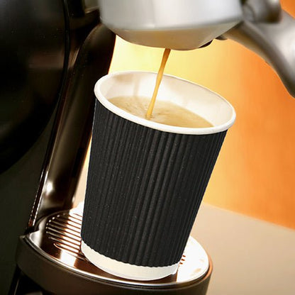 A Starpak 25 drinking cup, paper “To Go” Ripple Wall cup stands on a metal drip tray under the spout of a coffee machine, while hot coffee flows into it, standing out against a softly lit, warm-toned background.