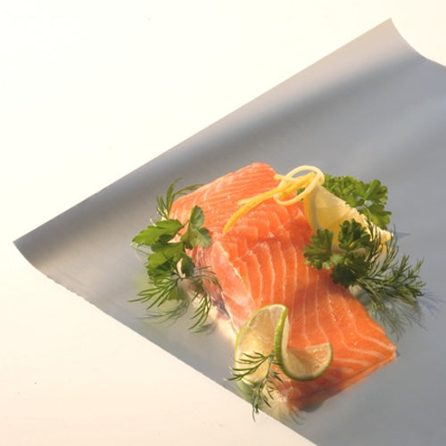A raw salmon fillet lies on Starpak aluminum foil in a folding box, garnished with lemon, lime, parsley, and dill – presenting the versatile uses of Starpak aluminum foil from Starpak against a light background.