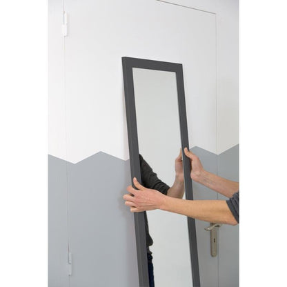 A person holds a rectangular mirror with a dark frame in front of a white door and patterned walls - perfect for mounting with Scotch-FIX™ Mirror Mounting Tape 4496W from 3M Deutschland GmbH.