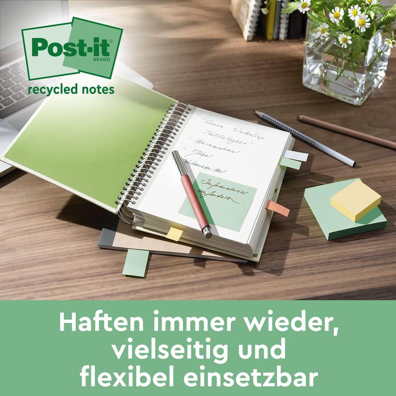 Tá deasc le leabhar nótaí oscailte ina bhfuil nóta glas Post-it® Super Sticky 100% Athchúrsáilte (76x76 mm, 70 bileog/bloc, 100% PEFC) ón 3M Deutschland GmbH, timpeallaithe le nótaí greamaitheacha, peann, cupán peann agus vása gloine. Téacs: "Greamaíonn siad arís agus arís eile.