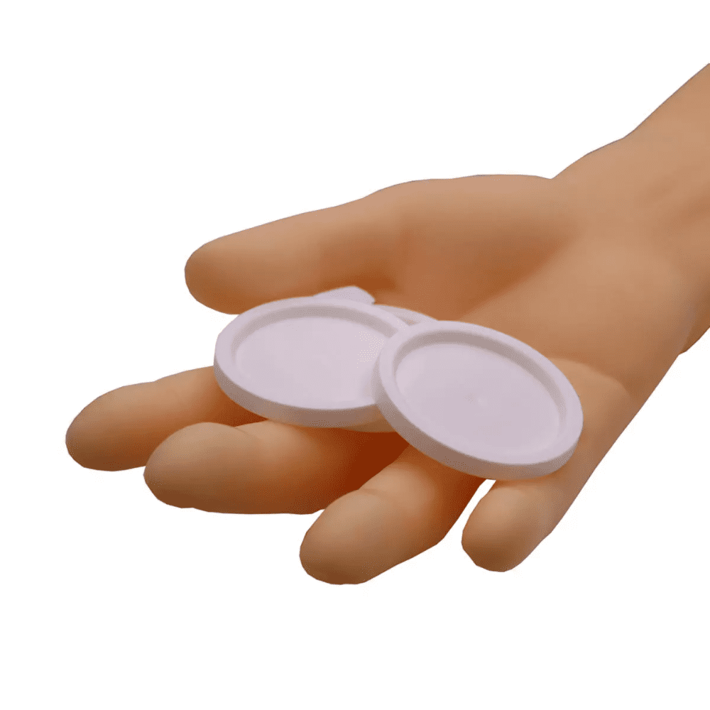 Tá lámh ag coinneáil dhá chlúdach cruinn AMPri do chupáin leighis, rudaí bána os comhair cúlra bán simplí.