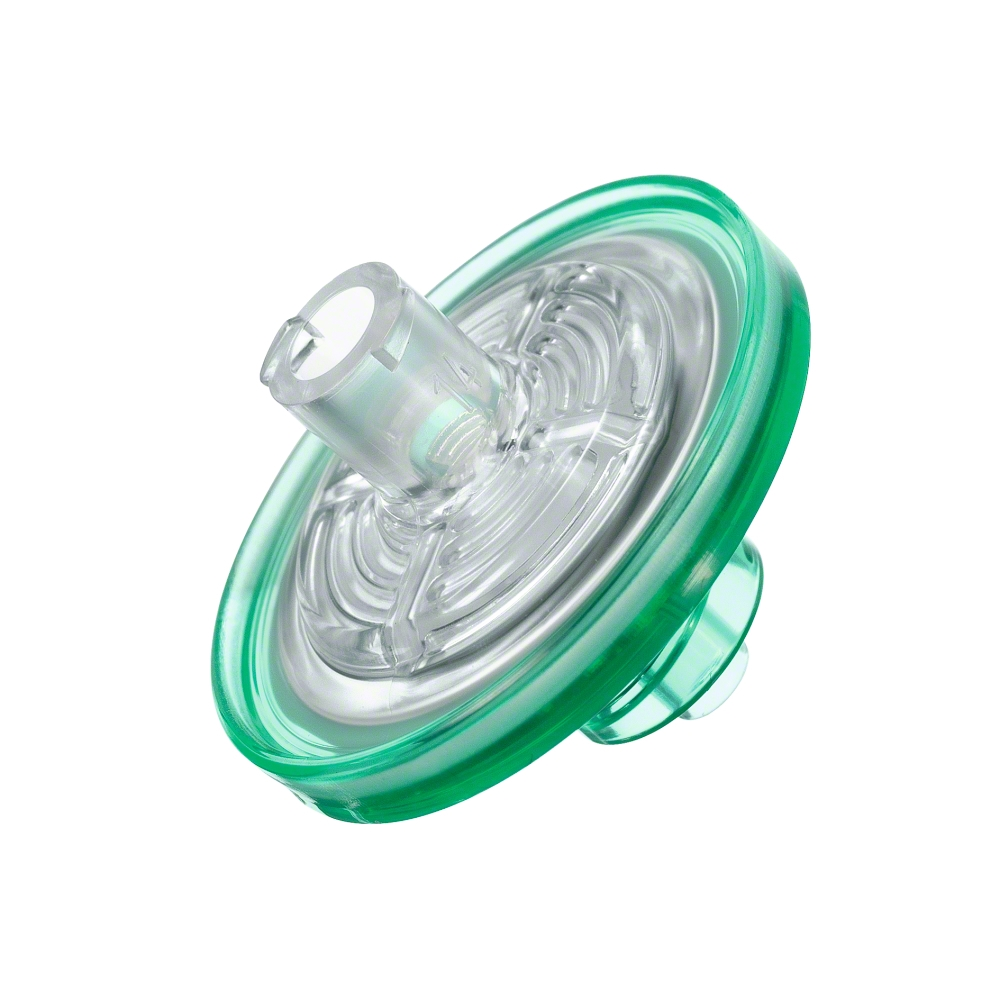 A close-up of the B.Braun Sterifix® injection filter, manufactured by B. Braun Deutschland GmbH & Co. KG, shows a round, transparent, green plastic filter that is often used in clinical applications. It has a central cylindrical connection and a round base. The design includes several visible layers through its transparent material to prevent bacterial contamination.