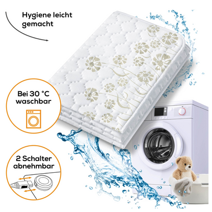 Das Bild zeigt ein Beurer Doppel-Wärmeunterbett UB 68 XXL | Packung (1 Stück) der Beurer GmbH, geschmückt mit floralen Motiven und einer gesteppten Matratzenauflage. Der Text weist darauf hin, dass es pflegeleicht, bei 30°C waschbar und mit zwei separat regelbaren Wärmezonen ausgestattet ist. Eine Waschmaschine mit Wasserspritzern und ein Teddybär sind ebenfalls Teil der visuellen Präsentation.
