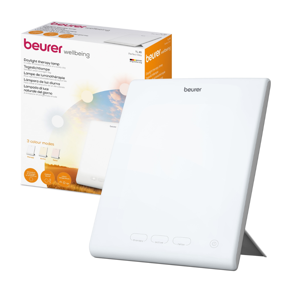 A white Beurer Perfect Day daylight lamp TL 45 by Beurer GmbH is shown next to its packaging. On the packaging, the product name and description can be found in several languages, with different color temperature modes displayed. The lamp has a simple design with buttons on the front, making it ideal for regulating your day-night rhythm.