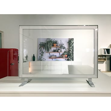 A Novocal hygiene protection wall straight without pass-through (transparent, 1,200 x 600 mm) with metal edges stands on a white surface; behind it, a wall shelf with plants, on the left a red refrigerator.
