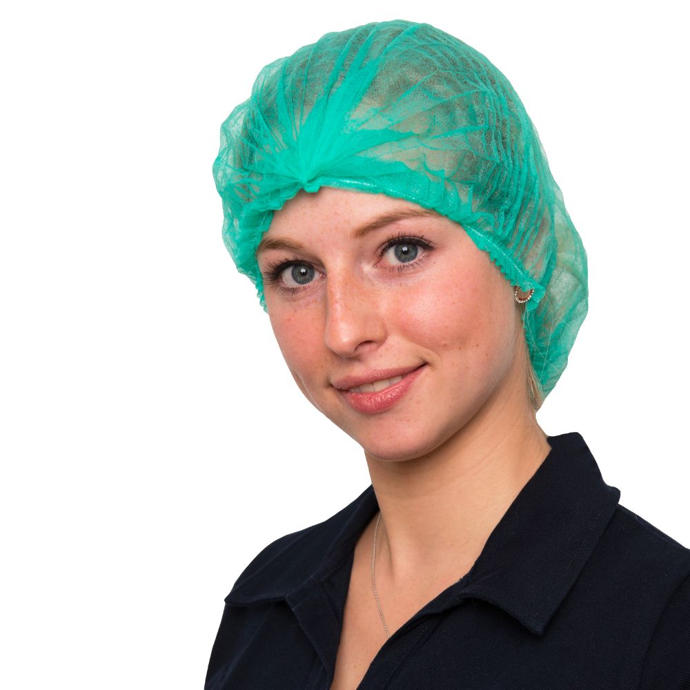 A person in a black shirt and a green disposable MCD MEDICAL CARE DENTAL GmbH NITRAS clip cap in green, 55 cm | Box (10 bags) smiles at the camera. The background is plain white.