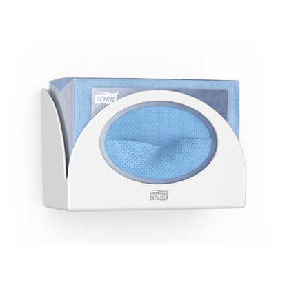 Ein Tork 655100 Small Pack Papierspender Performance W8 von Tork - Essity Professional Hygiene Germany GmbH, der hygienischen Schutz bietet, hält einen Stapel blauer Einwegtücher. Ein Tuch ist teilweise durch die Öffnung des Spenders gezogen. Das „Tork“-Logo ist sowohl auf dem schlanken Spender als auch auf der Verpackung der Tücher deutlich zu sehen.