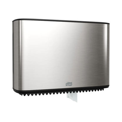 Tá dáileoir Tork Xpress do pháipéar leithris Mini-Jumbo, cuid den Image Line, suite go galánta ar an mballa. Tá dearadh caol dronuilleogach ag an dáileoir seo as cruach dhosmálta, agus tá cuid bheag de pháipéar bán le feiceáil ag an mbun. Tá an branda 'TORK – Essity Professional Hygiene Germany GmbH' le feiceáil go soiléir ar an tosaigh.