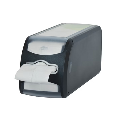 A black plastic countertop napkin dispenser Tork Xpressnap Fit® 272901 from TORK - Essity Professional Hygiene Germany GmbH features a transparent front part displaying a stack of white napkins, one of which protrudes through the opening. Its design allows for single sheet dispensing and is placed on a white background.