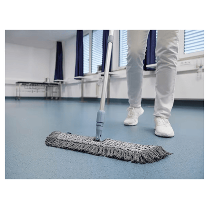 A person in white shoes and pants is mopping a blue floor with a Vileda GmbH Professional Swep Duo r-MicroCombi Mop - 50 cm in a room with closed blinds and blue curtains. A folding table stands nearby and a radiator is under the windows.