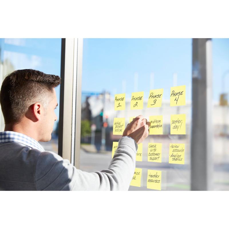 A person arranges handwritten project phases like "Phase 1" and "Interim Presentation" on a window with the Post-it® Super Sticky Z-Notes, Yellow (76x127mm, 90 sheets/block), PEFC-certified in cardboard packaging from 3M Deutschland GmbH.