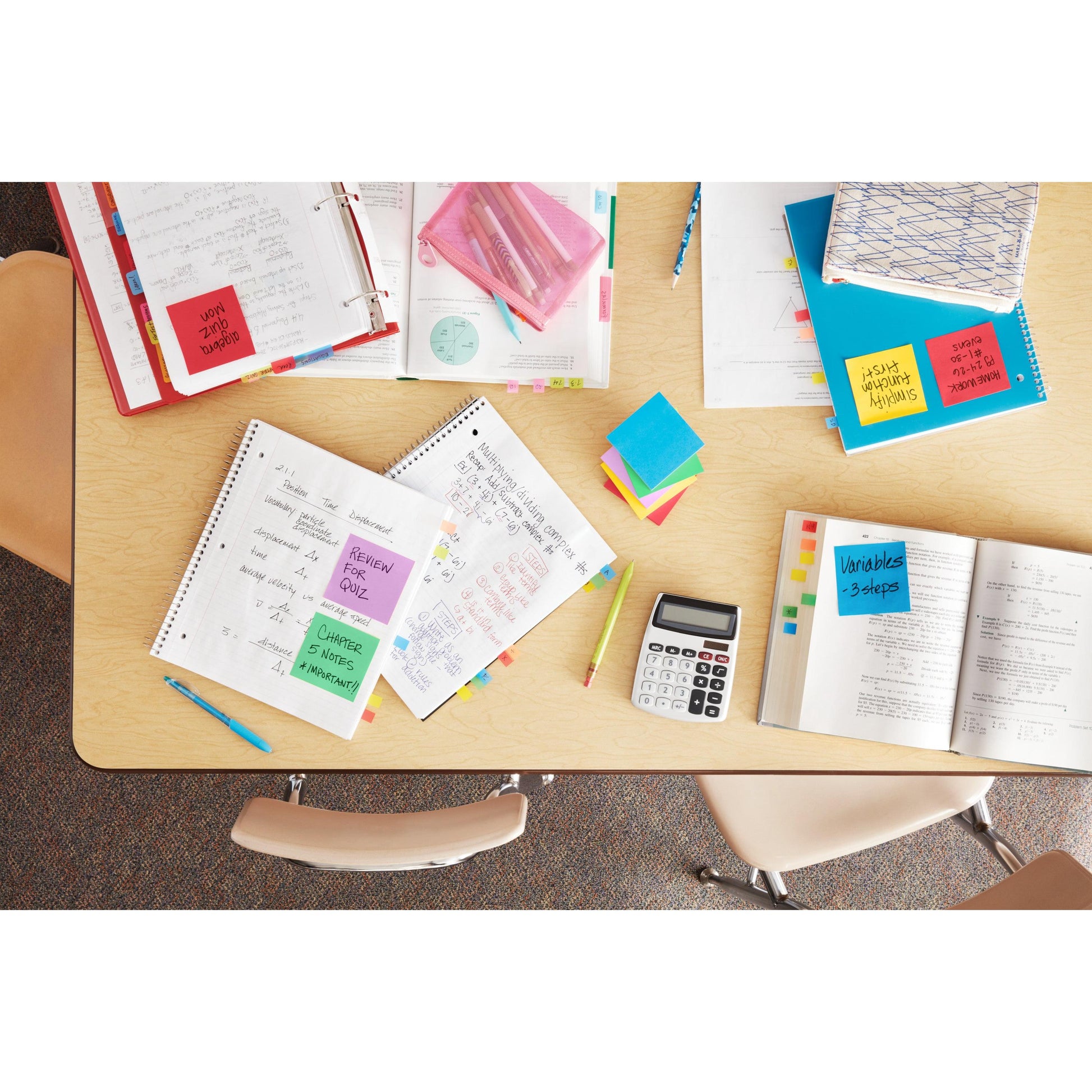 Auf einem Tisch im Klassenzimmer liegen aufgeschlagene Hefte, ein Taschenrechner, Bleistifte, Mappen und die Post-it® Notes Energetic Collection (76x127 mm, 100 Blatt/Block, 6 Blöcke/Packung) der 3M Deutschland GmbH. Zwei leere Stühle sind am Tisch aufgestellt.