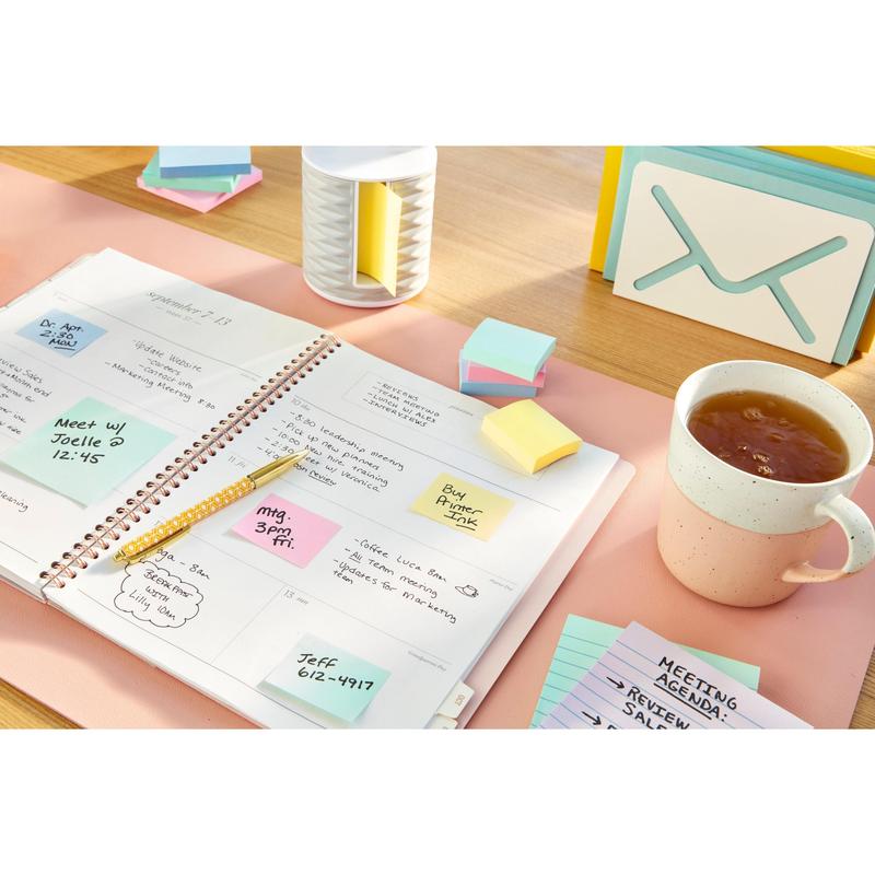 On a desk lie a planner with Post-it® Recycling Z-Notes (Yellow, 76x76mm, 100% PEFC) from 3M Deutschland GmbH, a pencil, a tea cup, a stack of index cards, a small storage box, and a container shaped like an envelope.