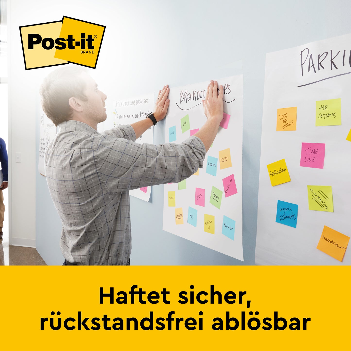 Ein Mann drückt ein Blatt Papier mit bunten Post-it-Zetteln an eine Wand und präsentiert dabei das 3M Deutschland GmbH Post-it® Super Sticky selbsthaftendes Meeting Chart/Flipchart für Wand-Montage 566 (58,4 x 50,8 cm, 20 Blatt, 2 Blöcke, inkl. Command™-Streifen).