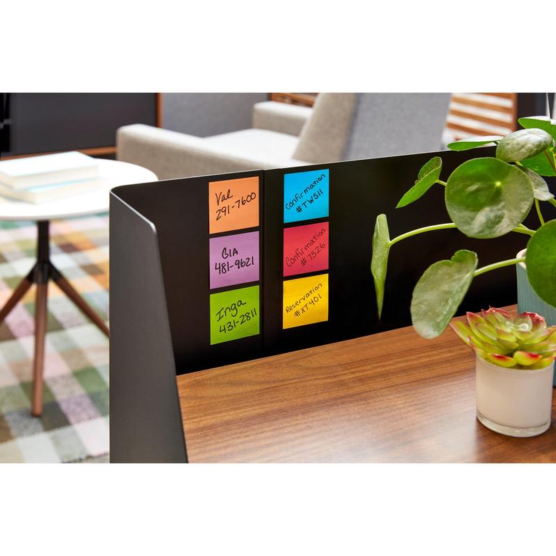 A black metal divider on a wooden table displays six packs of 3M Deutschland GmbH Post-it® Notes, Yellow, 76x76mm, 90 sheets/block, PEFC-certified. Green potted plants adorn the desk, with books and a chair in the background.