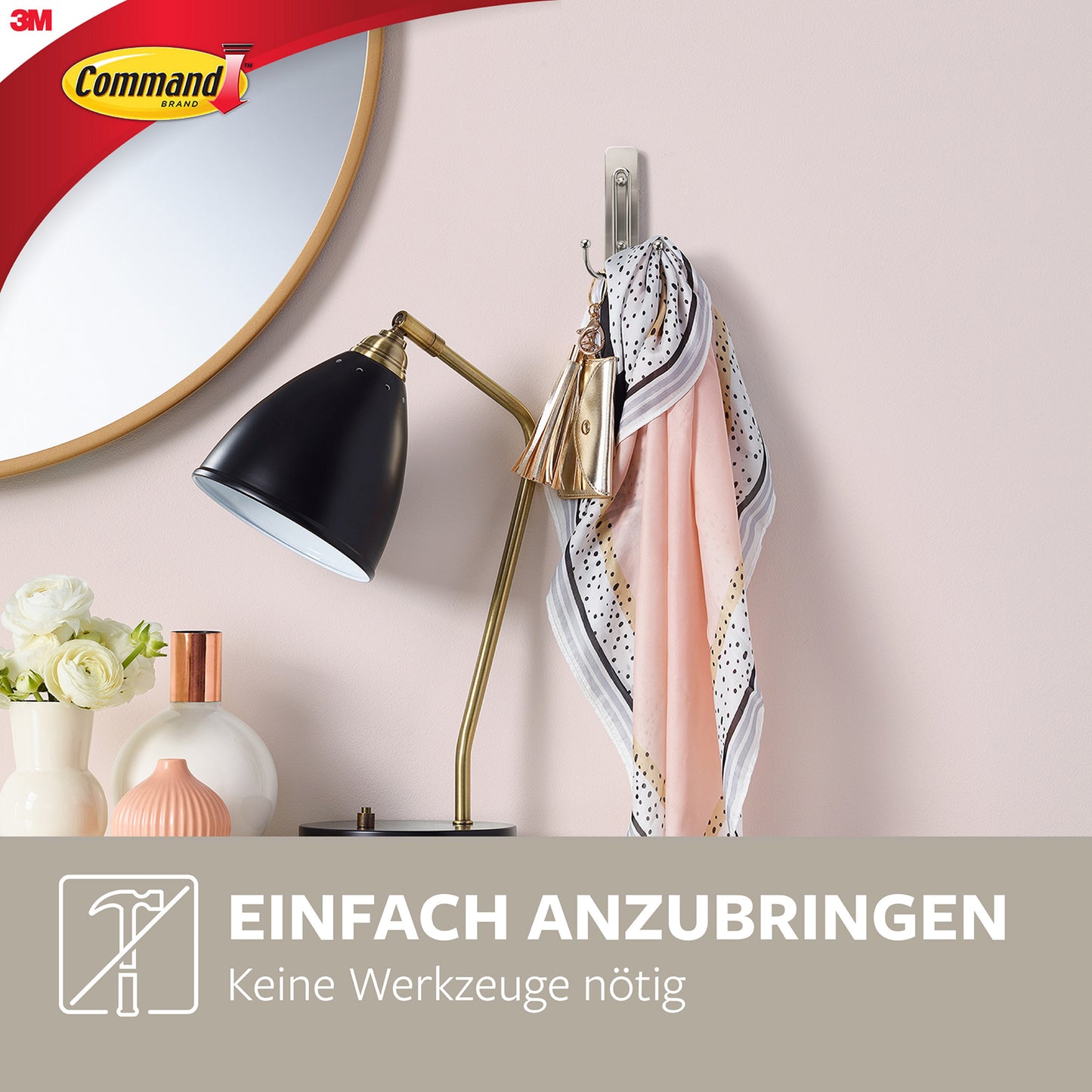 Ein Schal und ein Schlüsselanhänger hängen an einem großen Command™ Doppelhaken in gebürstetem Nickel (17036, 1 Haken, 1 Strip) von 3M Deutschland GmbH, montiert an einer rosa Wand über Lampe und Vasen. Logo oben links. Text: "Einfach anzubringen. Keine Werkzeuge nötig.