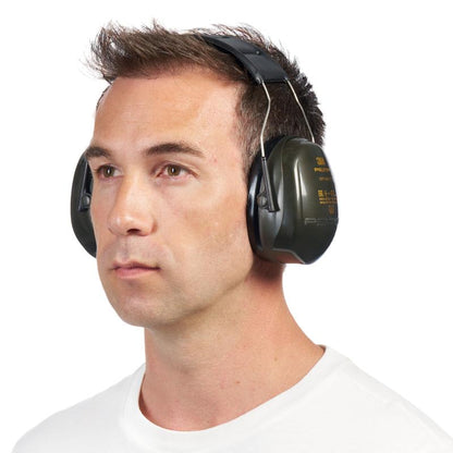 Fear le gruaig ghearr dhonn, i léine bhán shimplí, ag caitheamh 3M™ PELTOR™ Optime™ II H520A Cluasáin mhóra ghlasa (SNR 31 dB, 1 Píosa) ó 3M Deutschland GmbH, beagán dírithe ar chlé ar chúlra bán.