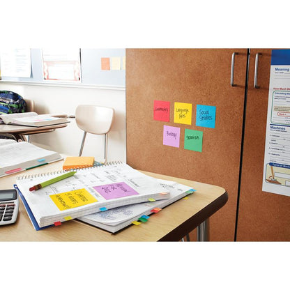 On a classroom desk are open notebooks, papers, a calculator, and Post-it® Super Sticky Notes (76 x 127 mm, 90 sheets/block, 100% PEFC) from 3M Deutschland GmbH. Colorful notes with subject labels are attached to a cabinet nearby.